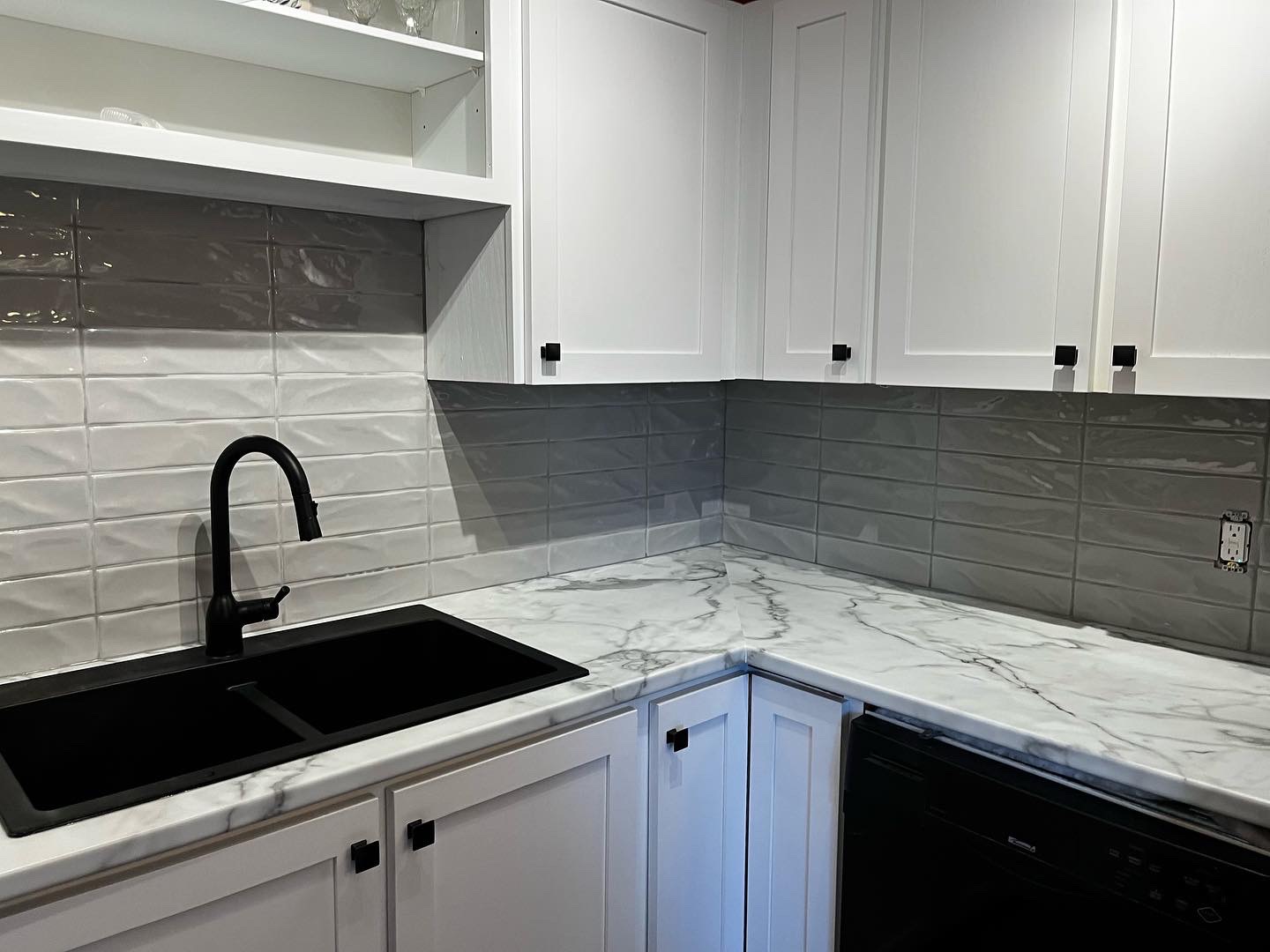 A grey tile backsplash over a calacatta laminate countertop with ablack granite sink and white cabinets creates a very modern kitchen look